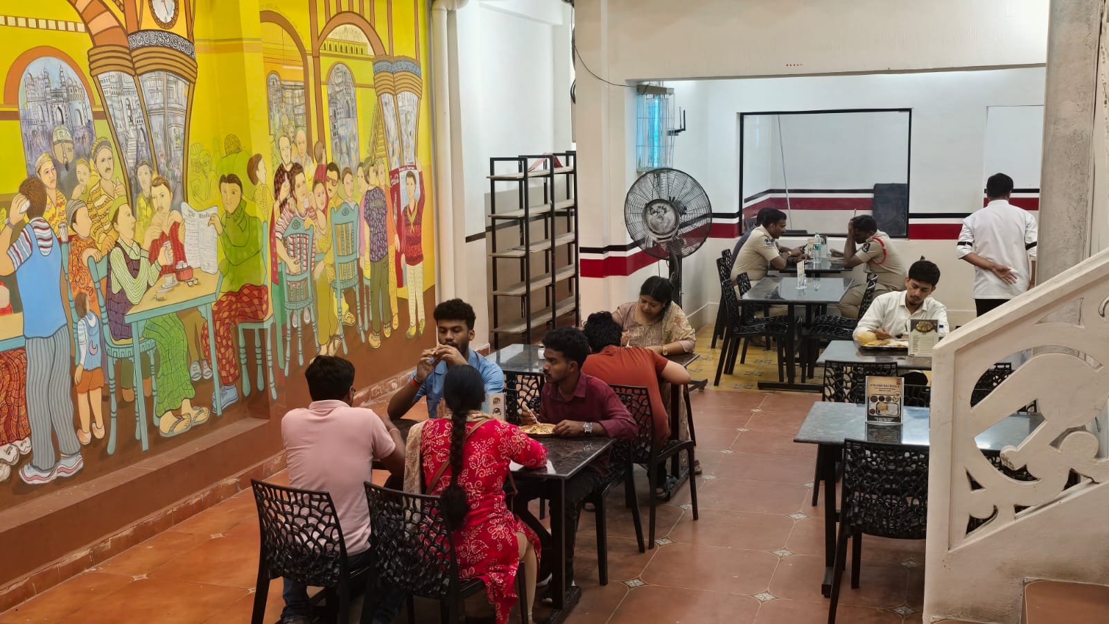 Guests eating South Indian breakfast on the walk-in ground floor at Kaapi & Karam near Charminar, beside a full-height mural of an Old City coffee house
